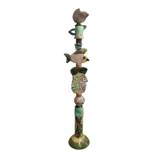 Juxtaposition 2 Ceramic Totem – hand-built ceramic totem by Zimmerman with small bird at top, large fish spreading wide in purple, gold, and black stripes, teal and purple geometric face below, bold black and gold abstract base marks from printmaking vocabulary